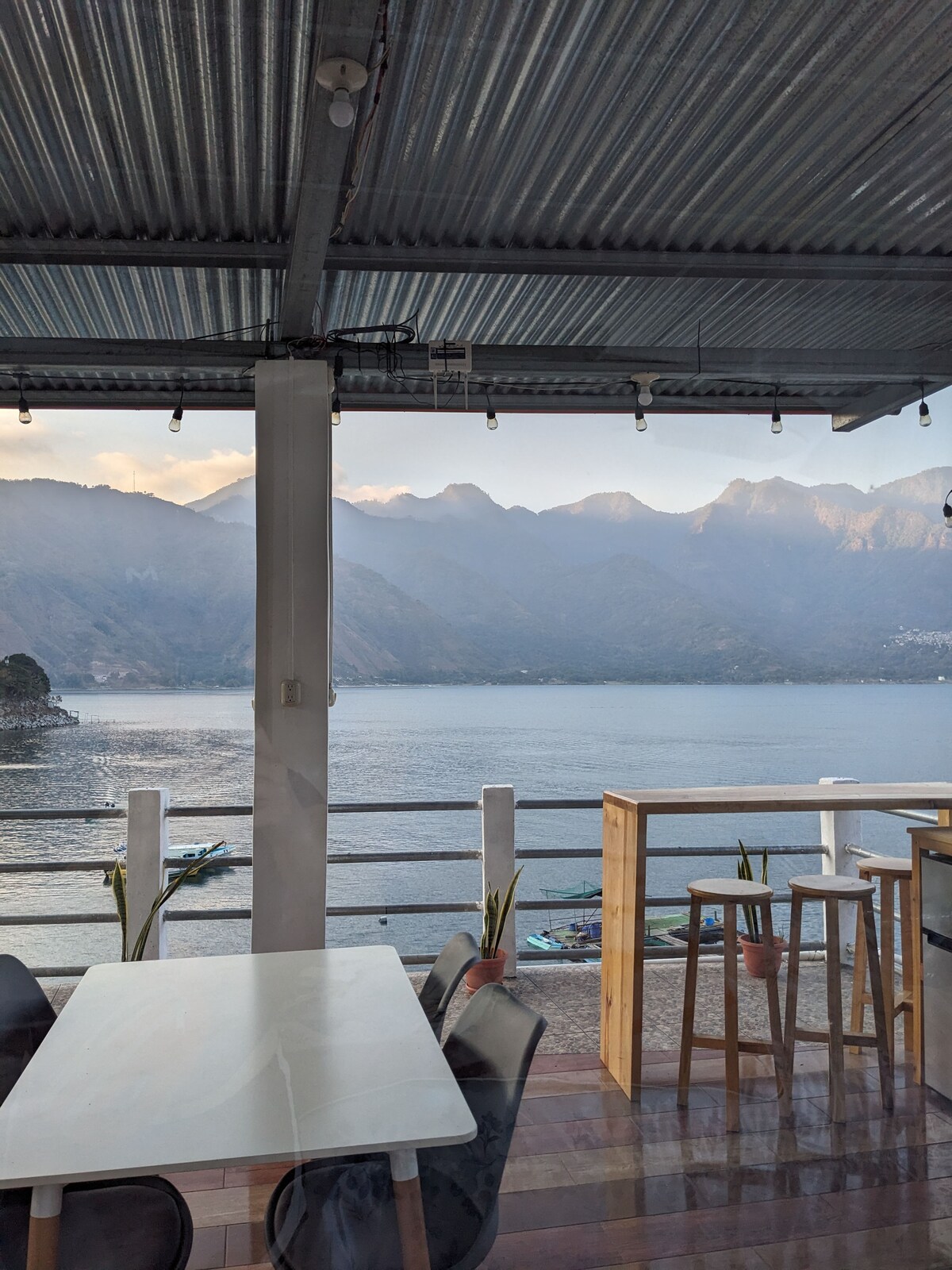 An outdoor kitchen and living area features a dining table and chairs positioned to maximize the stunning views of the lake and surrounding mountains. Natural light floods the space, enhanced by the modern design of the covered rooftop terrace.