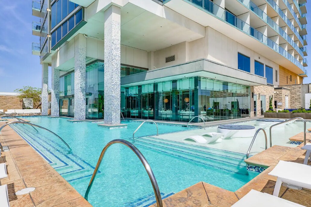 A modern resort-style pool area is highlighted, featuring sleek lines and a refreshing turquoise water surface. Sun loungers are arranged around the pool, and a relaxation area with integrated spa elements is visible, complementing the building's contemporary architectural design.