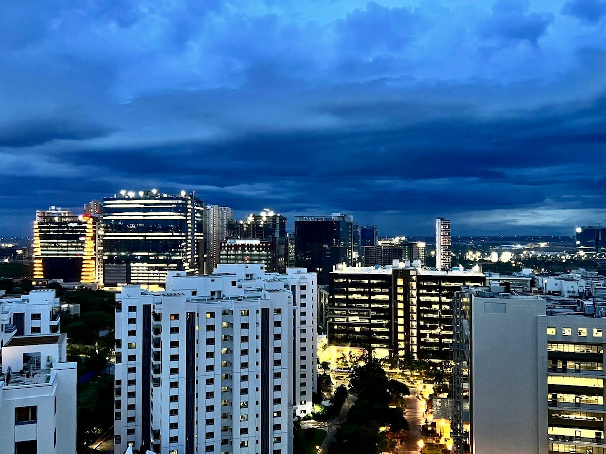 A cityscape view showcases modern high-rise buildings illuminated against a twilight sky. The scene highlights contrasting architectural designs and the glow of streetlights below, offering a glimpse of urban life in the vibrant neighborhood.