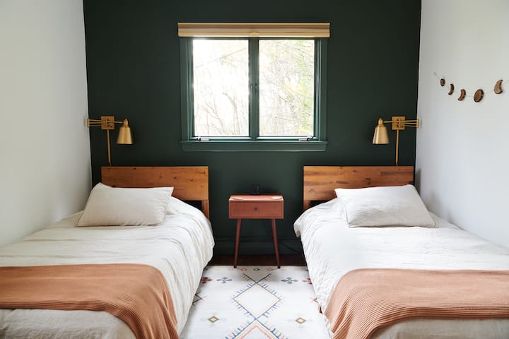 Მყუდრო ორადგილიანი საძინებელი ტყის ხედით. Მუქი მწვანე აქცენტის კედელი, ხის თავსაბურავები და ხრაშუნა თეთრი თეთრეული. Ოქროს კედელი წასაკითხად. Ბუნებრივი სინათლე დიდი ფანჯრებიდან. Იდეალურია ორი ბავშვისთვის ან ზრდასრულებისთვის ძალიან კომფორტული და მშვიდი სივრცე.