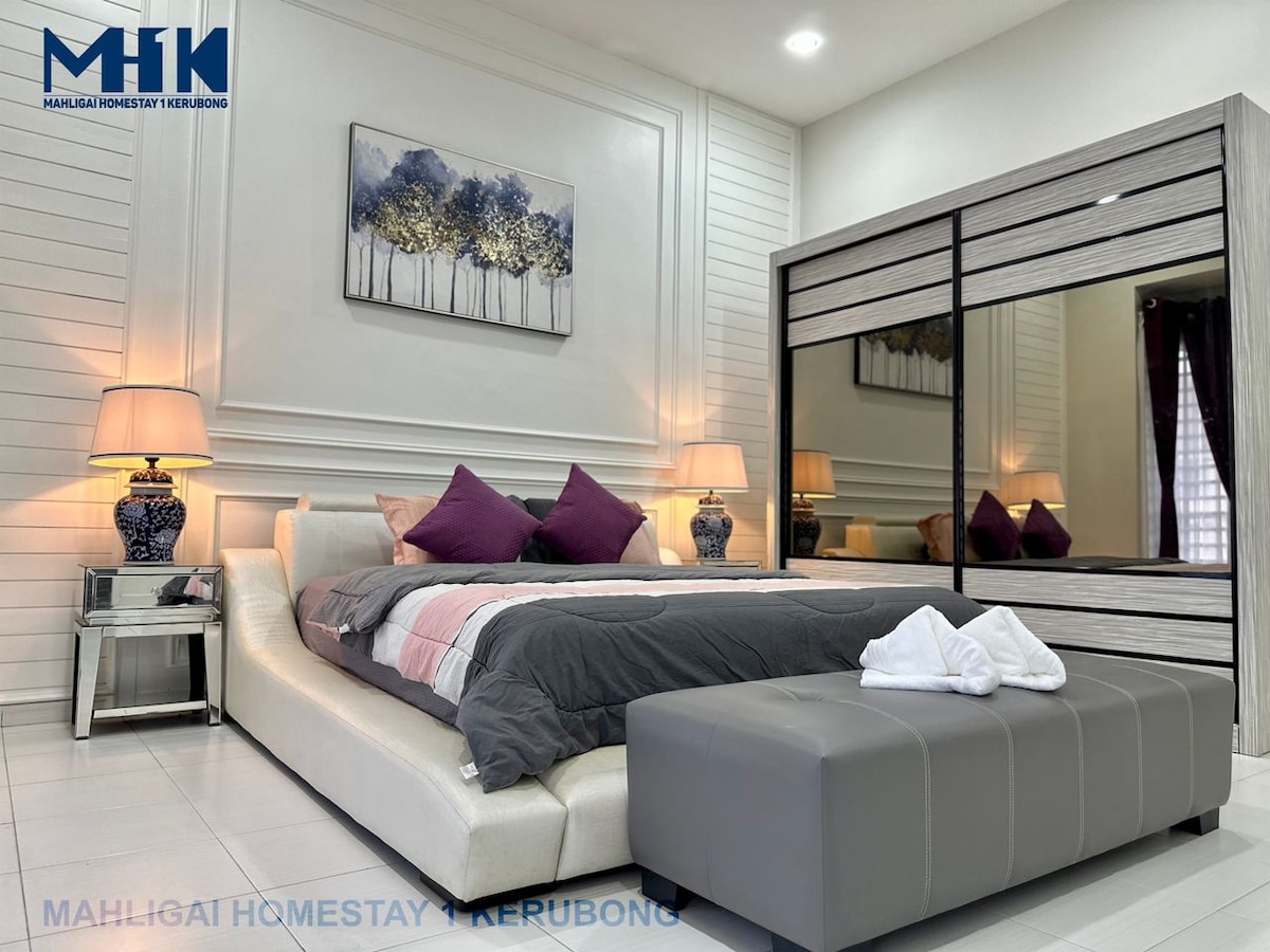 A contemporary bedroom features a spacious bed with neutral bedding and decorative purple accents. A mirrored wardrobe complements the room's modern design, while a piece of wall art adds a subtle touch of elegance. Natural light softly illuminates the space.