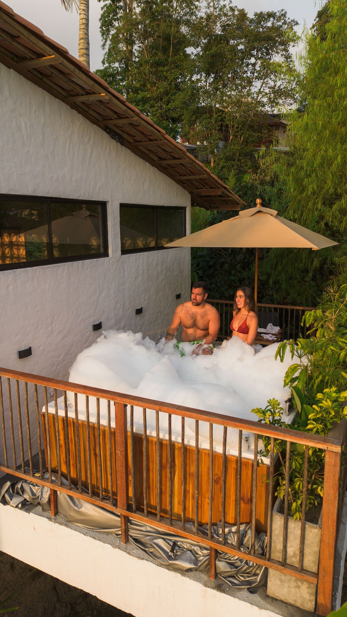 A private jacuzzi is set on a spacious deck surrounded by lush greenery. The warm bubble bath creates a serene atmosphere. Soft sunlight filters through the trees, providing a tranquil environment for relaxation.