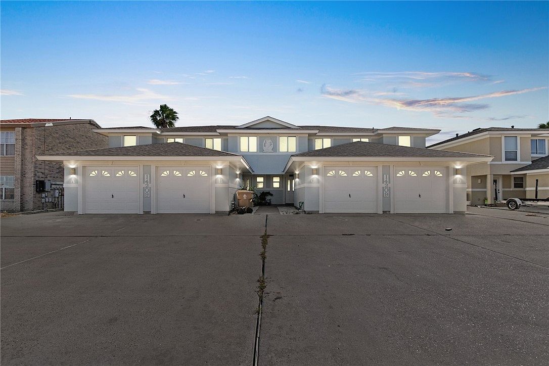 The townhome exterior features a well-maintained façade with multiple garage doors, each equipped with decorative windows. The driveway provides ample space, leading up to the entrance. The structure is framed by clear blue skies, indicating a tranquil atmosphere.
