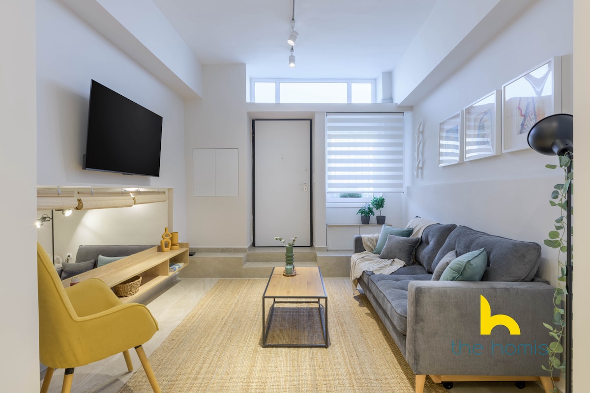 The spacious living area features a comfortable sofa and a bright yellow armchair, providing a cozy seating arrangement. A minimalist wooden coffee table sits on a textured rug, while natural light streams in through the window, enhancing the inviting ambiance.