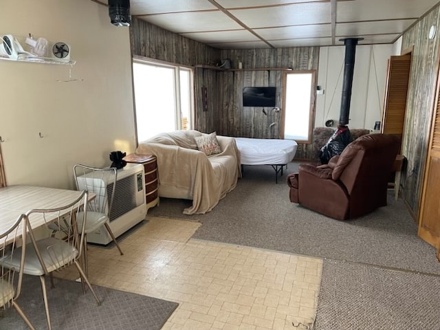 A functional living space is showcased with a light-colored couch and a convertible bed, complemented by a brown armchair. Large windows provide natural light, while a small dining table and chairs are positioned nearby. A heater and television are also present in the room.