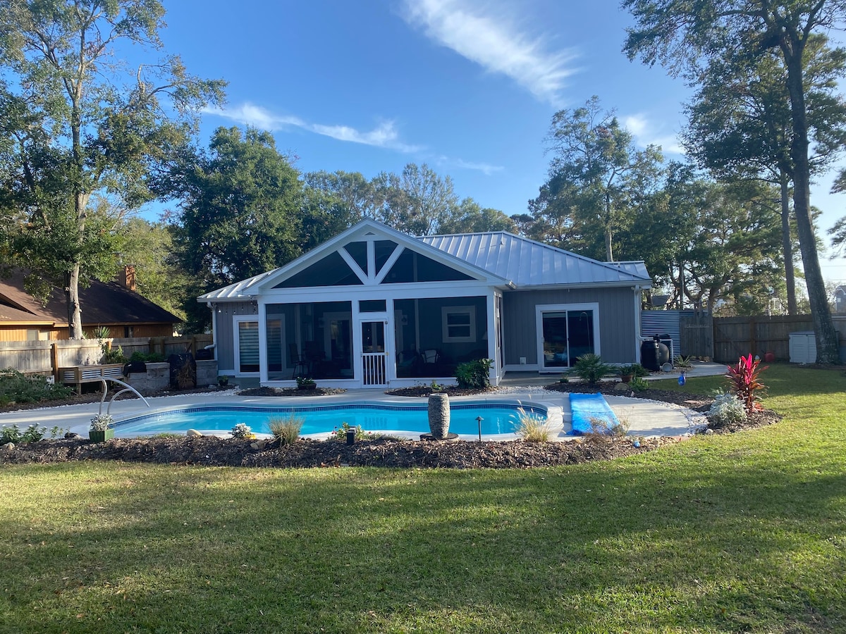 An expansive backyard features a private pool surrounded by landscaped greenery and garden elements. A modern home with a sloped roof is visible, showcasing large windows that invite natural light. A decorative fountain adds a serene touch to the outdoor space.