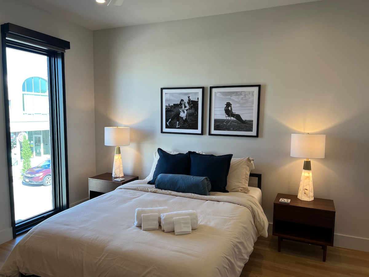 Primary bedroom showcases new artwork, a queen bed, floor-to-ceiling windows for natural light, and an attached bathroom for added convenience.