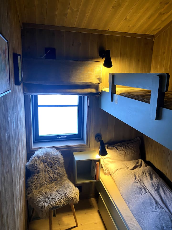 Спалната соба на југоистокот на викендичката има кревет на спрат со скала, ноќни масички и светилки за читање. 