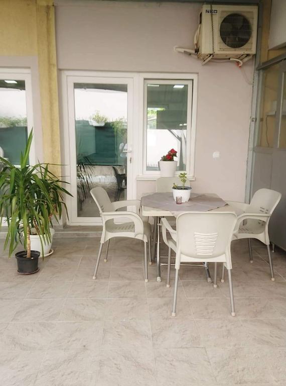 A patio area is featured with a round dining table and four lightweight chairs. Potted plants add a touch of greenery, and large windows allow natural light to fill the space. An air conditioning unit is mounted above, ensuring comfort.