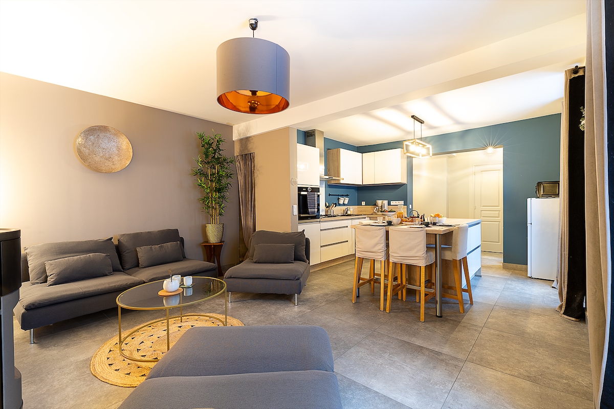 A modern living space is highlighted, featuring comfortable gray sofas arranged around a circular coffee table. The open kitchen, equipped with contemporary appliances, is designed for social gatherings. A neutral color palette enhances the bright atmosphere, complemented by warm lighting from a stylish pendant.