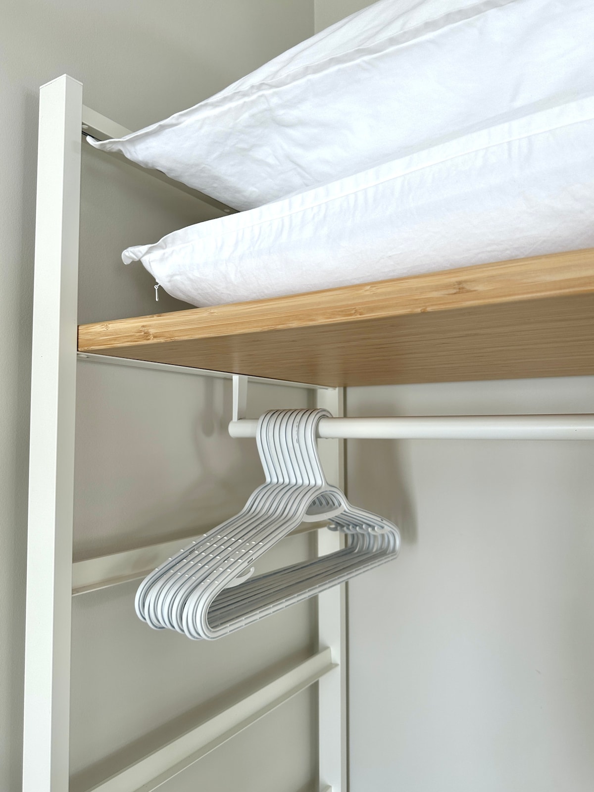 A closet space features a wooden shelf above with a neatly arranged white comforter. Below, multiple light grey hangers are hanging from a metal rail, providing easy access for clothing storage.