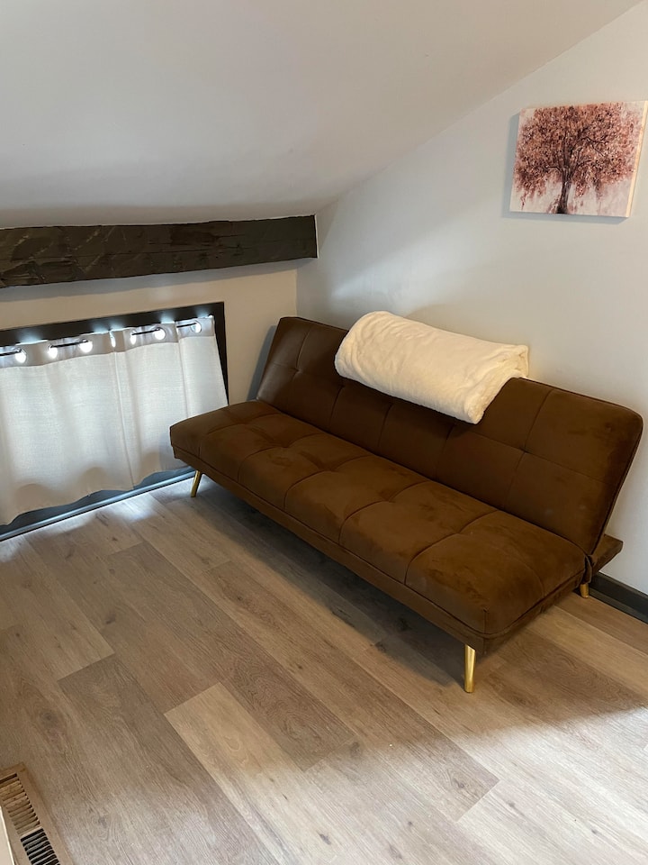 Отворен простор за седење на горниот кат со кауч на спуштање,  мал телевизор на ѕидот за детска зона. Ова не е приватна спална соба зад врата.