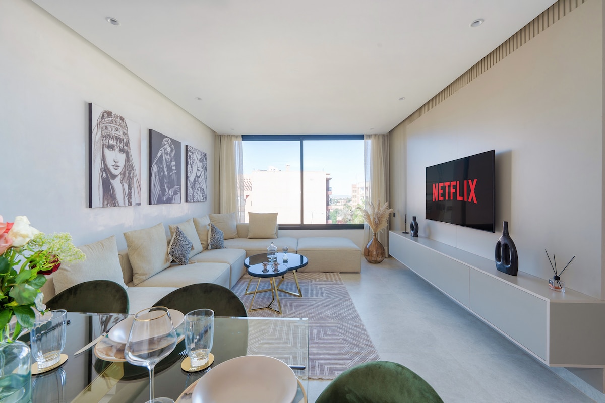A modern living space is shown, featuring a comfortable fabric sofa and a stylish coffee table. A large window allows natural light to illuminate the room, while a sleek entertainment unit displays a smart TV. Decorative elements, including vases, enhance the contemporary design.