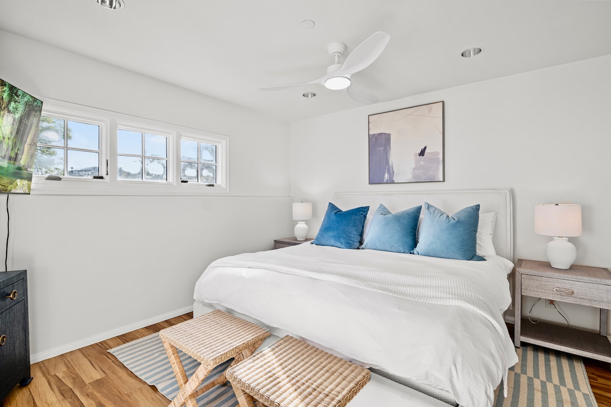 למטה חדר שינה עם מיטת קינג סייז ונוף לאוקיינוס, דלתות זכוכית המובילות לפטיו, טלוויזיה, ארונות וחדר רחצה צמוד.