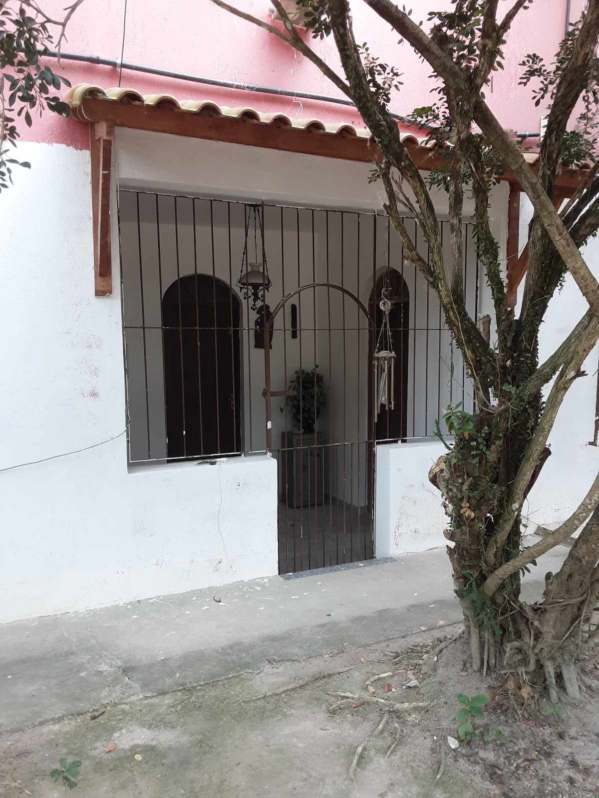 The entrance to the suite is framed by a simple iron gate, allowing views of the courtyard. Two arched windows are visible, with decorative elements hanging adjacent to the entrance. A small plant is positioned inside, adding a touch of greenery.