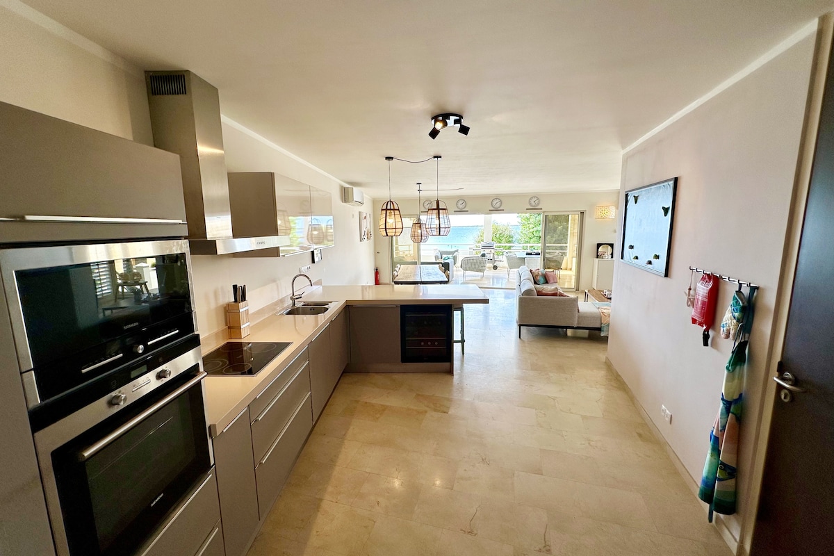 The spacious kitchen features modern appliances including an oven, microwave, and an induction cooktop. Sleek cabinetry provides ample storage. Natural light fills the area, with views extending to the living space and balcony beyond, enhancing the openness of the design.