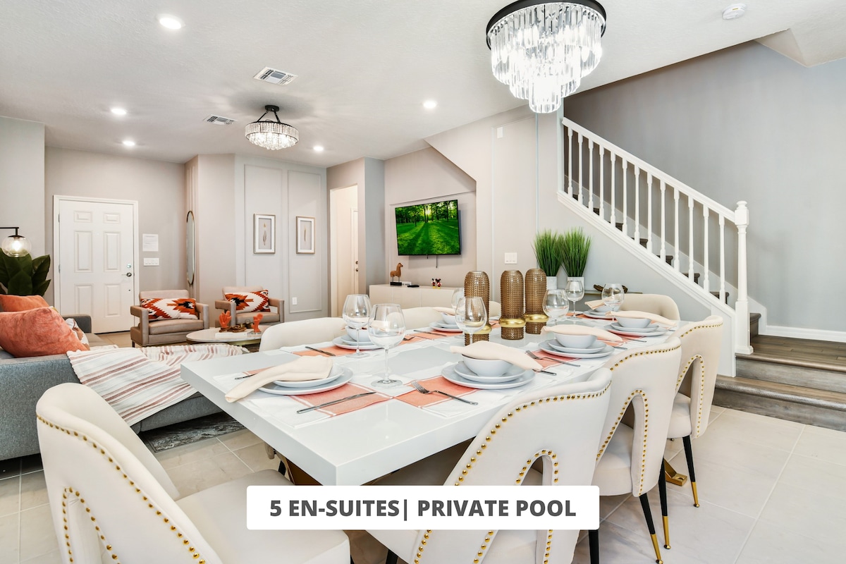 A spacious dining area is equipped with a large table set for a meal, surrounded by elegant chairs. The open-concept design connects to a comfortable living area, featuring soft lighting and a television. A staircase leads to the upper level, enhancing the inviting atmosphere.