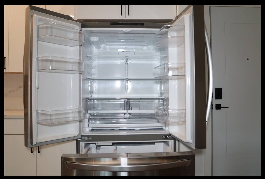 A modern refrigerator is shown with its doors opened wide. The interior features multiple clear shelves and compartments, providing ample storage space. The design includes a bottom freezer drawer. The overall color scheme is silver, complementing the sleek kitchen aesthetics.