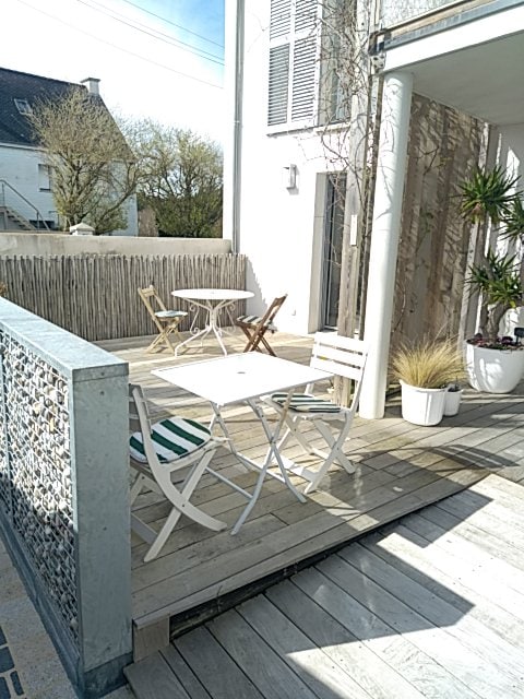 A wooden terrace is shown, featuring a small round table and two folding chairs. Potted plants add greenery to the space, while the surrounding fencing offers privacy. Natural light illuminates the area, creating an inviting spot for outdoor meals or relaxation.