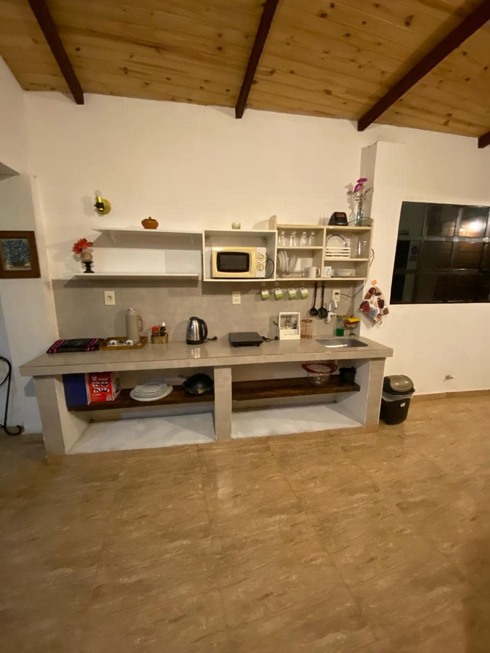 The kitchen area features a modern countertop with essential appliances, including a microwave and kettle. Open shelves display dishware, while a large window allows natural light, creating a functional and inviting cooking space.