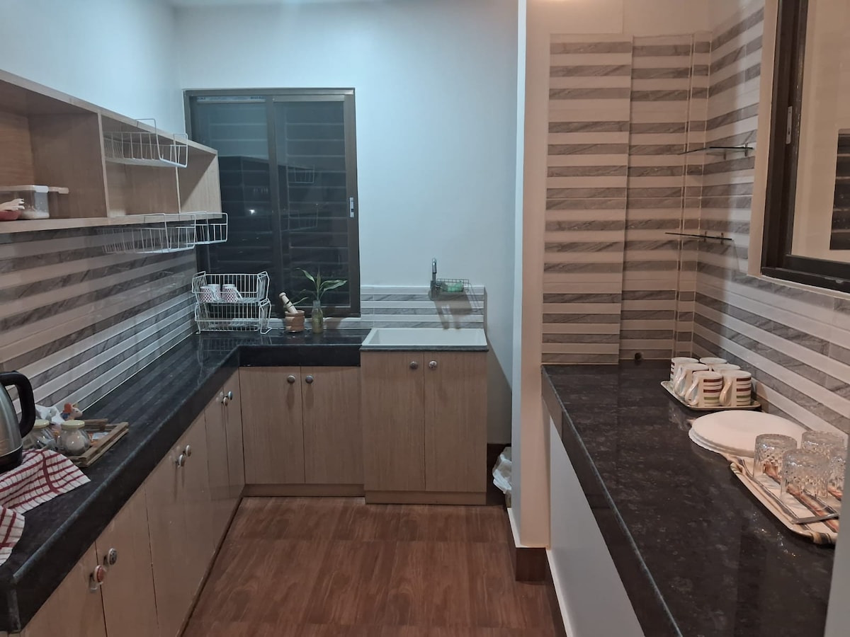 A modern kitchen is presented, featuring wooden cabinets and a dark countertop. The space includes a sink under a window, with a dish drying rack nearby. Decorative elements are arranged on the countertop, complemented by striped wall patterns that add a subtle texture.