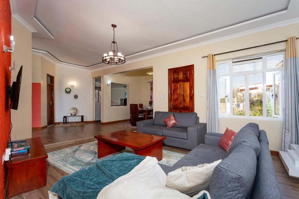 A spacious living area is presented with a combination of comfortable seating, including a gray sofa and an armchair. A wooden coffee table sits in the center, while light pours in through the large windows adorned with soft curtains. An open layout allows visibility into the dining area.