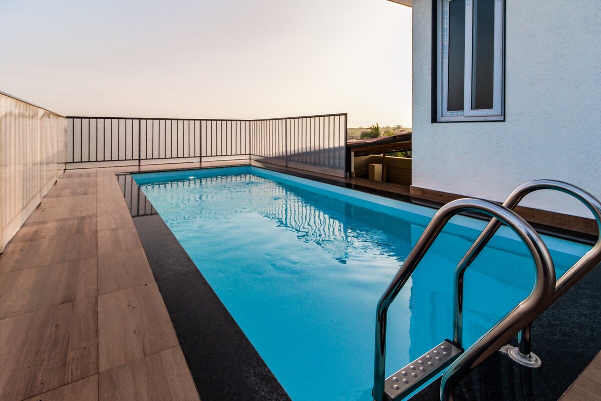 A serene pool area features a sleek, rectangular pool with clear water, complemented by stylish metal handrails. A surrounding deck provides ample space for relaxation, and the distant horizon offers a glimpse of the sky, enhancing the calm ambiance of the retreat.