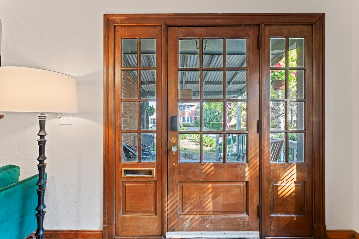 A wooden front door features multiple glass panes, providing a bright entry while allowing views of the outdoors. A standing lamp is positioned nearby, casting a soft glow in the inviting space.