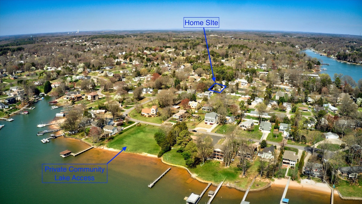 An aerial view captures the surrounding residential area near the lake. The scene highlights the layout of homes, green spaces, and access points to the private community lake. The tranquil water reflects the lush landscape, indicating proximity to boating and recreational areas.