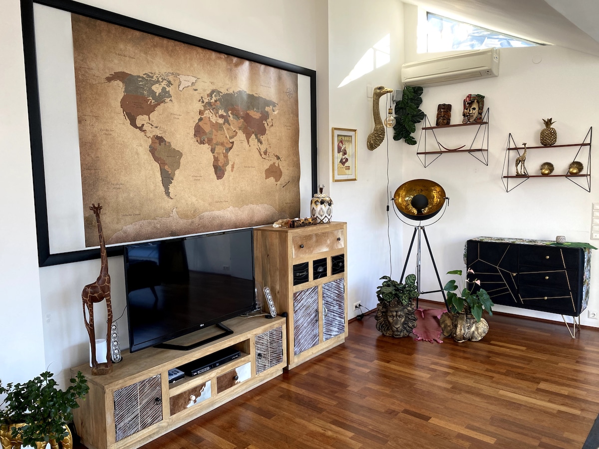 A living area features a large world map on the wall, complementing the natural wood tones of the floor. A flat-screen TV is positioned on a wooden cabinet with woven details. Decorative pieces include a globe and plants, adding a touch of nature to the space.