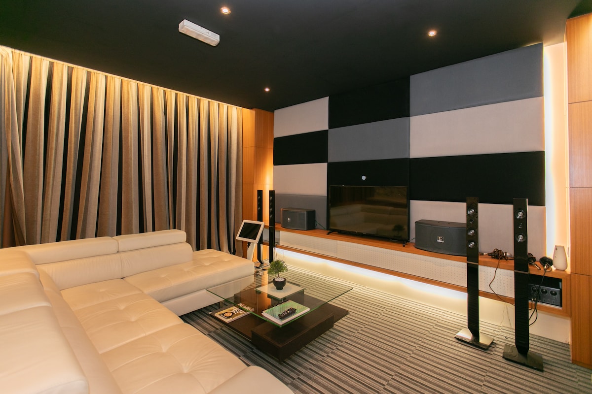 A comfortable entertainment area is furnished with a white sectional sofa. A coffee table sits at the center, accompanied by ambient lighting that highlights the textured wall. A flat-screen television is mounted on the wall, flanked by audio speakers for an enhanced viewing experience.