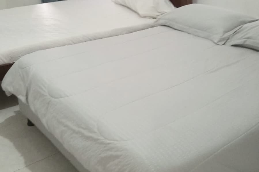 The sleeping area features a spacious bed covered with a light-colored quilt. A second bed is positioned nearby, both beds are adorned with simple white linens. Soft lighting illuminates the room, enhancing a relaxed and comfortable setting.