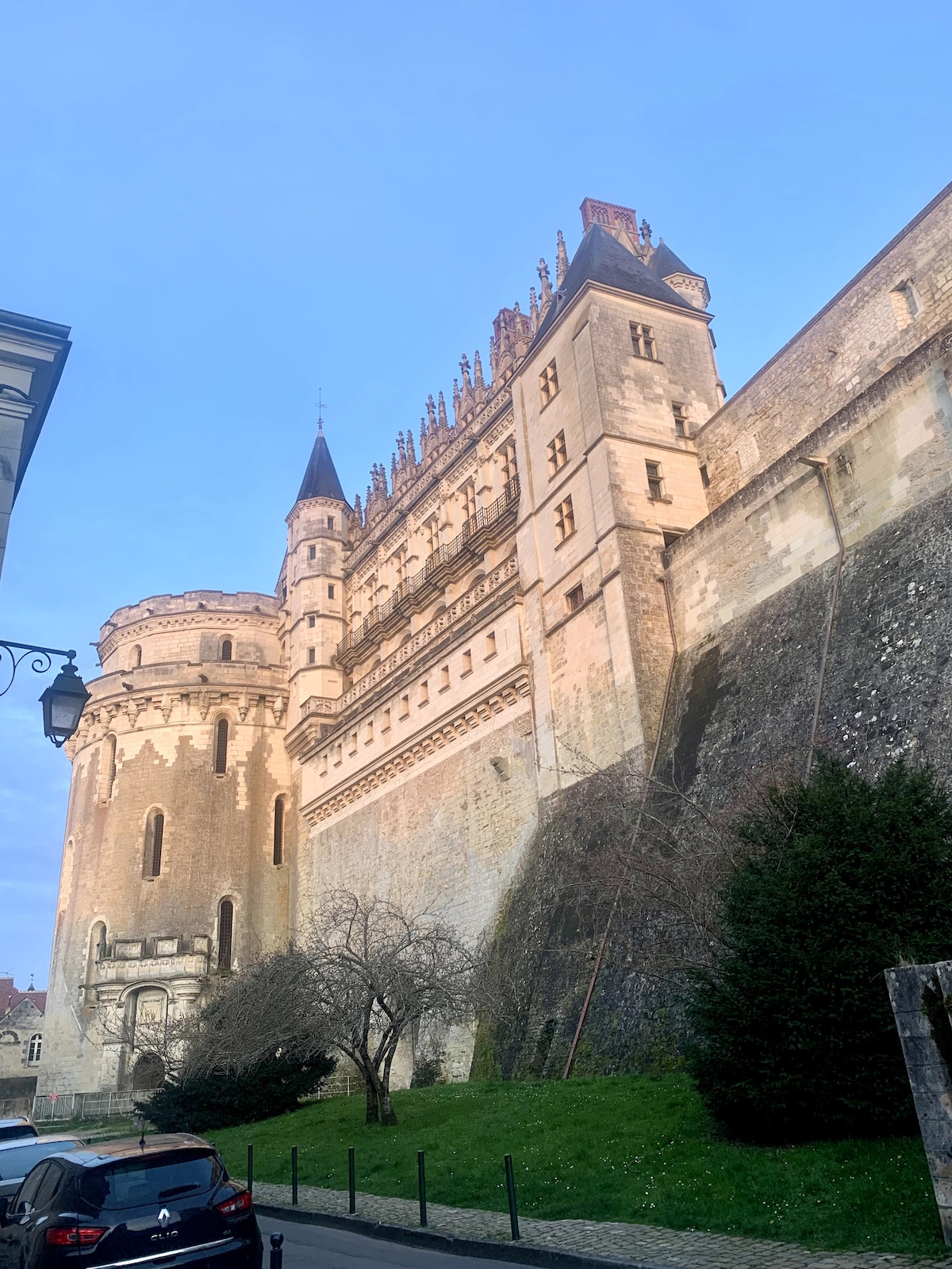 The image captures the impressive side view of a historic castle, showcasing its ornate architecture and towering spires. The well-preserved stone walls contrast with the lush greenery in the foreground, while the soft light of dusk illuminates the structure.