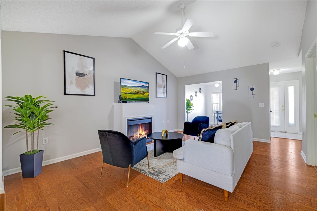 A bright living area is present, featuring a light-colored sofa and two dark chairs. A fireplace adds warmth, while a flat-screen TV is mounted on the wall. Natural light enters through nearby windows, enhancing the spacious atmosphere.