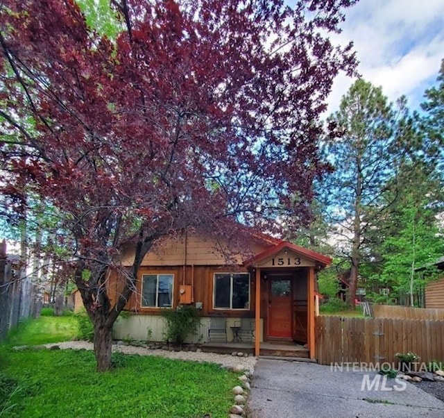 A charming wooden home showcases its inviting front entrance framed by a lush garden. A vibrant maroon tree stands prominently in the forefront, with a gravel path guiding guests to the door. Natural greenery surrounds the property, enhancing its connection to the outdoors.