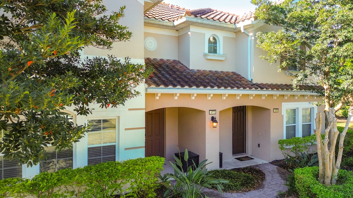 The exterior of the home features a charming entrance with a tiled roof and decorative window. Lush greenery surrounds the walkway, creating a welcoming first impression. The inviting front door is framed by two windows and is complemented by tasteful landscaping.