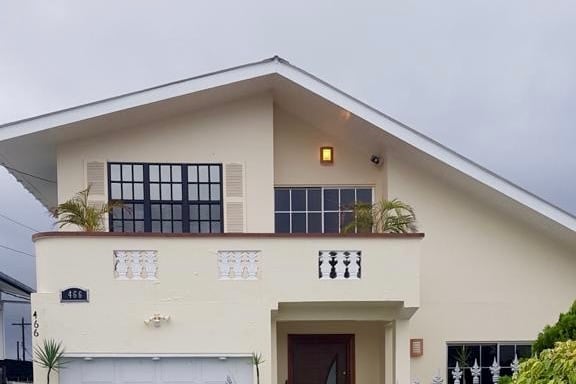 A modern two-story home is presented with a sloped roof and large windows allowing natural light to fill the space. The entryway is framed by plants, while the garage door is subtly integrated into the façade, providing an inviting appearance.