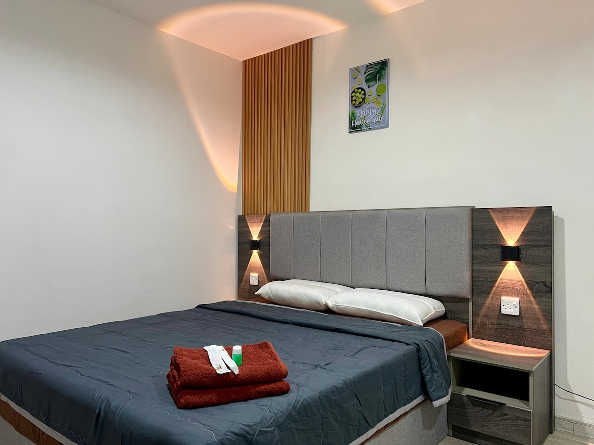 A modern bedroom is presented with a spacious bed adorned with crisp linens and neatly arranged pillows. Soft lighting accentuates the headboard, while a warm-colored blanket is placed at the foot of the bed. A framed artwork is displayed on the wall, adding a touch of decor.