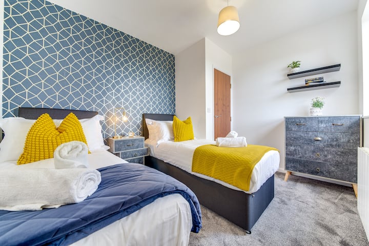 Светло, стилно място за отдих с две спални, ярка синя контрастна стена, слънчеви жълти акценти и уютни халати, идеално за групи или семейства.