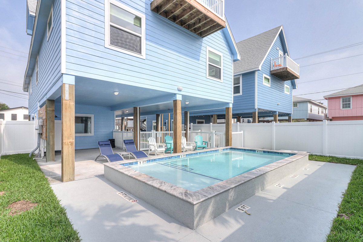 A private pool is framed by a spacious patio area, with ample lounge chairs provided for relaxation. The house features a blue exterior with wooden support posts and a fenced yard, creating a serene outdoor space just steps from the pool.