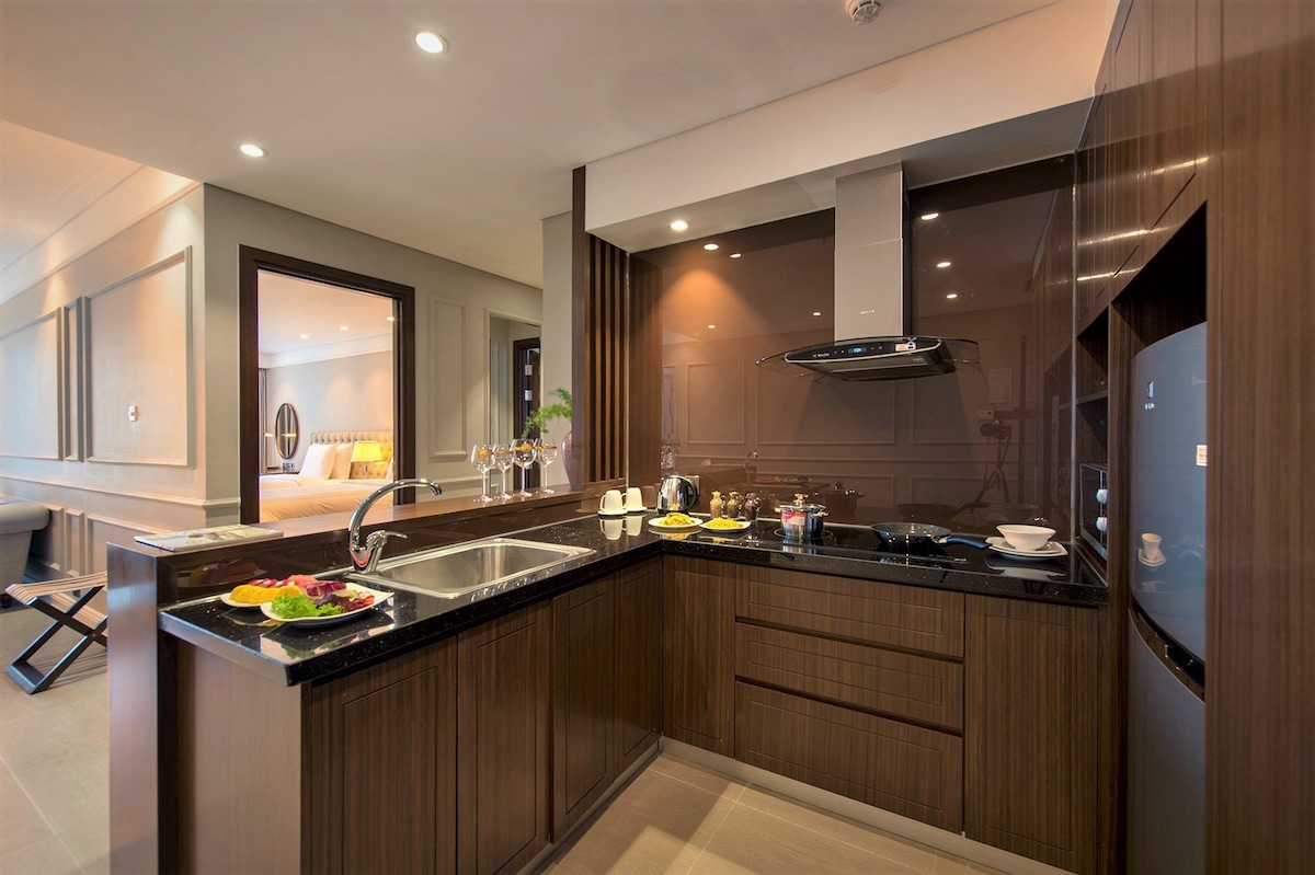 The kitchen area features sleek, dark wood cabinetry and a granite countertop. A double sink is positioned beside modern appliances, including a stove and a refrigerator. Dining essentials are arranged on the counter, providing a functional space for meal preparation.