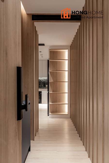 A stylish corridor is characterized by vertical wooden slats that create a sense of depth. Soft lighting accentuates the texture of the walls, while the entrance to the kitchen is visible at the far end, inviting guests to explore further.