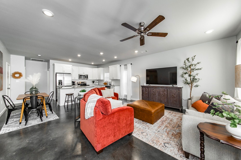 An open living area is featured with a mix of comfortable furnishings, including a red sofa and a neutral-toned couch. A ceiling fan watches over the space. A dark wooden cabinet and a dining table with chairs are visible, creating a cohesive and functional environment.