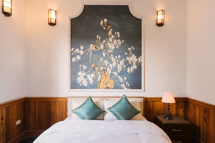 هذه غرفة نوم أصغر مع سرير متوسط الحجم وخزانة ملابس وطاولة جانبية مع كرسيين وتلفزيون وثلاجة صغيرة وأثاث آخر. الحمام في الداخل.