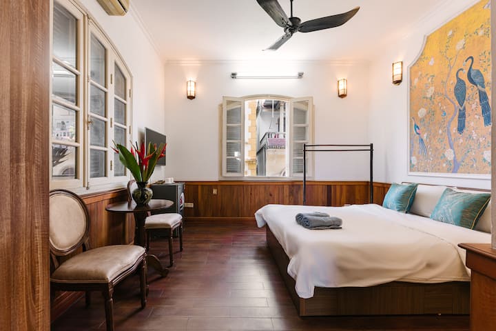 هذه غرفة نوم أصغر مع سرير متوسط الحجم وخزانة ملابس وطاولة جانبية مع كرسيين وتلفزيون وثلاجة صغيرة وأثاث آخر. الحمام في الداخل.