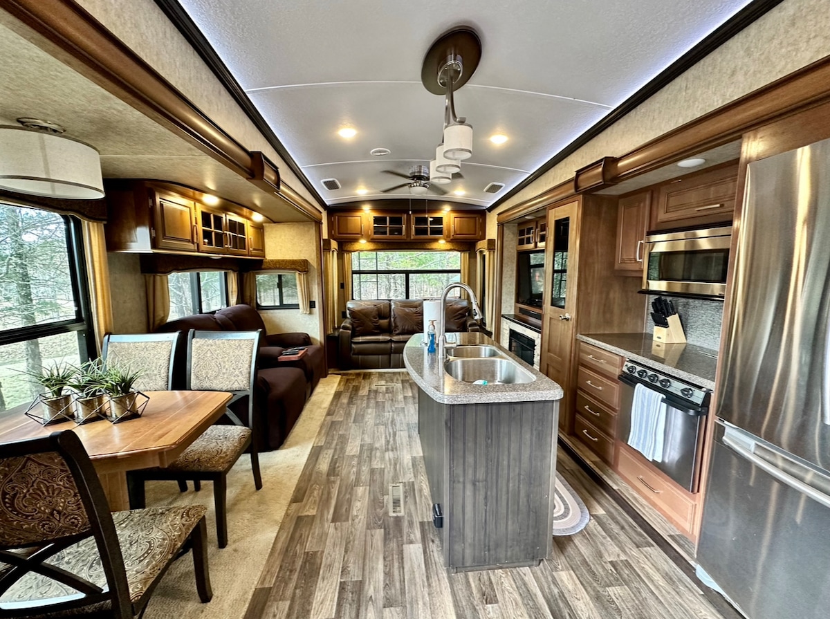 An inviting interior blends a modern kitchen with a dining area and living space. A central island with a granite countertop complements stainless steel appliances. Natural light fills the room through large windows, while a cozy sofa and dining table create a welcoming atmosphere.