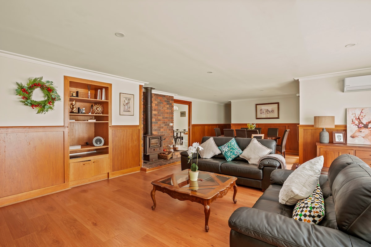 A spacious living area is designed with warm wood paneling and features a cozy seating arrangement. A wooden coffee table sits in the center, enhanced by a potted plant. A brick fireplace adds a rustic touch, while air conditioning is positioned for comfort.