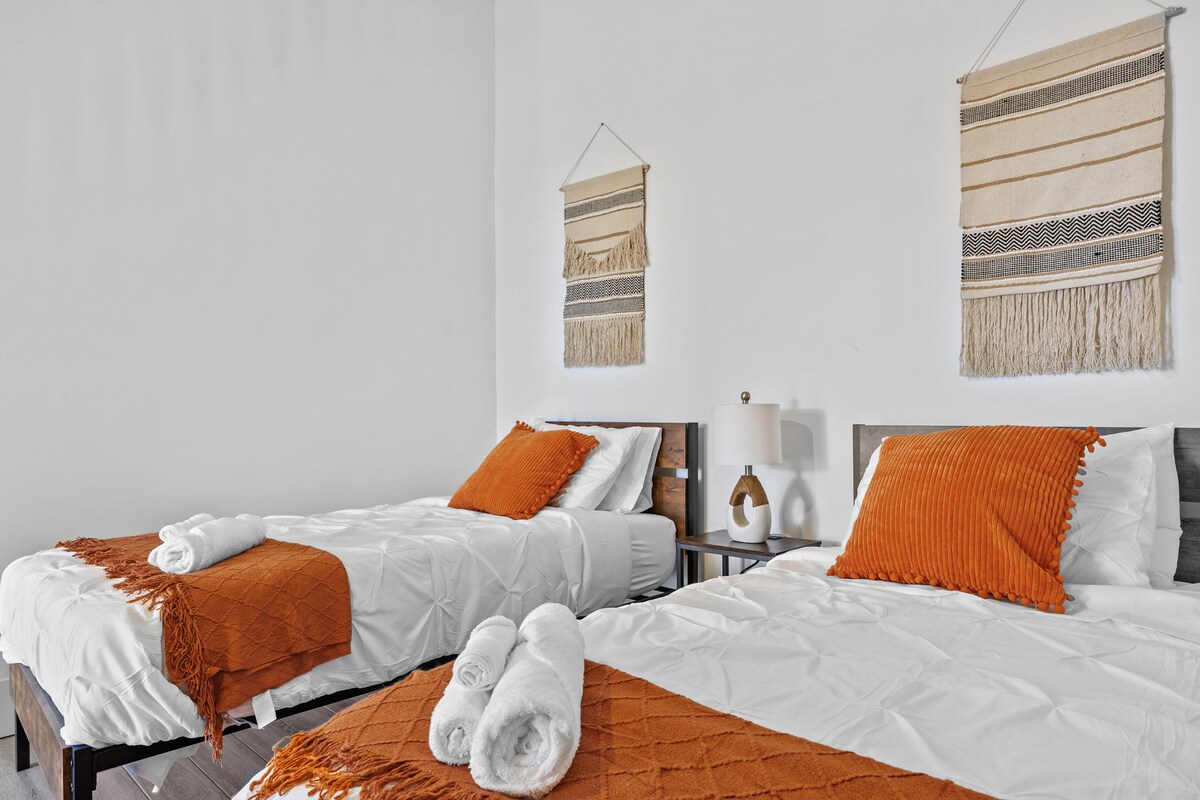 คุณจะได้เข้าสู่ห้องนอนที่อบอุ่นซึ่งออกแบบด้วยเตียงเดี่ยว 2 เตียงแต่ละเตียงตกแต่งด้วยผ้าปูที่นอนสีขาวที่คมชัดและประดับประดาด้วยสำเนียงสีส้มอบอุ่นที่ให้ความรู้สึกมีชีวิตชีวาแก่ที่พัก