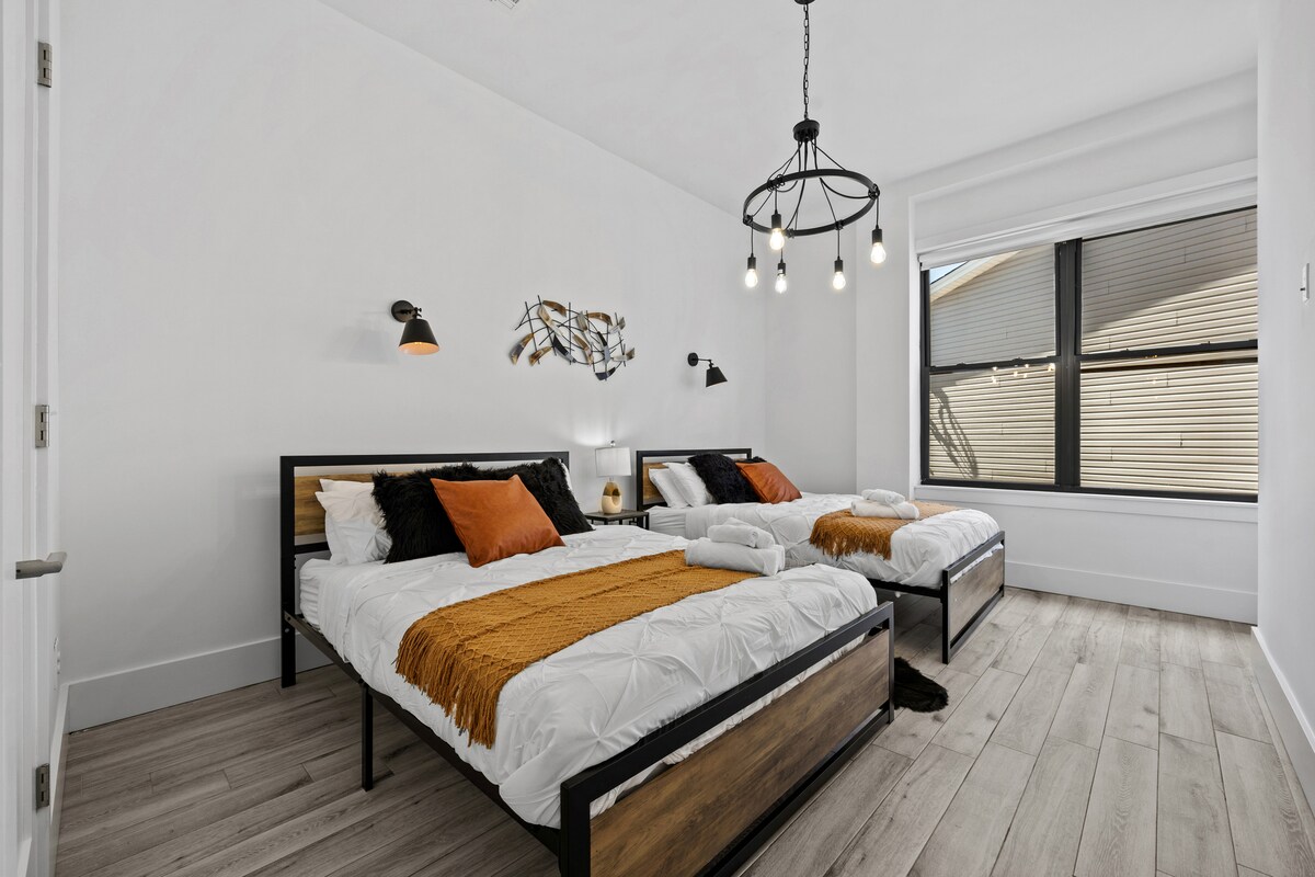 ห้องนอนมีสไตล์นี้เชิญคุณมาพร้อมเตียงขนาดควีนไซส์ 2 เตียงแต่ละเตียงตกแต่งด้วยผ้าปูที่นอนสีขาวหรูหราและเน้นด้วยหมอนสีส้มและสีดำที่มีชีวิตชีวาสร้างความรู้สึกอบอุ่นและน่าอยู่