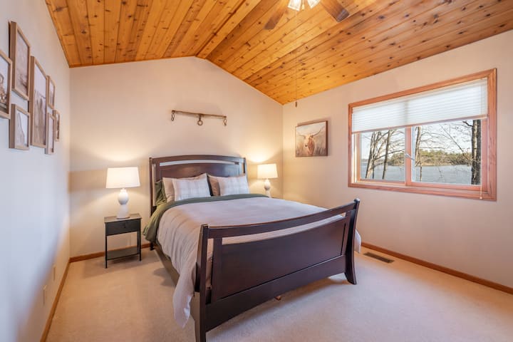Wake up to peaceful lake views in this cozy primary bedroom, featuring a plush queen bed, warm decorative touches, and a private en-suite bathroom.